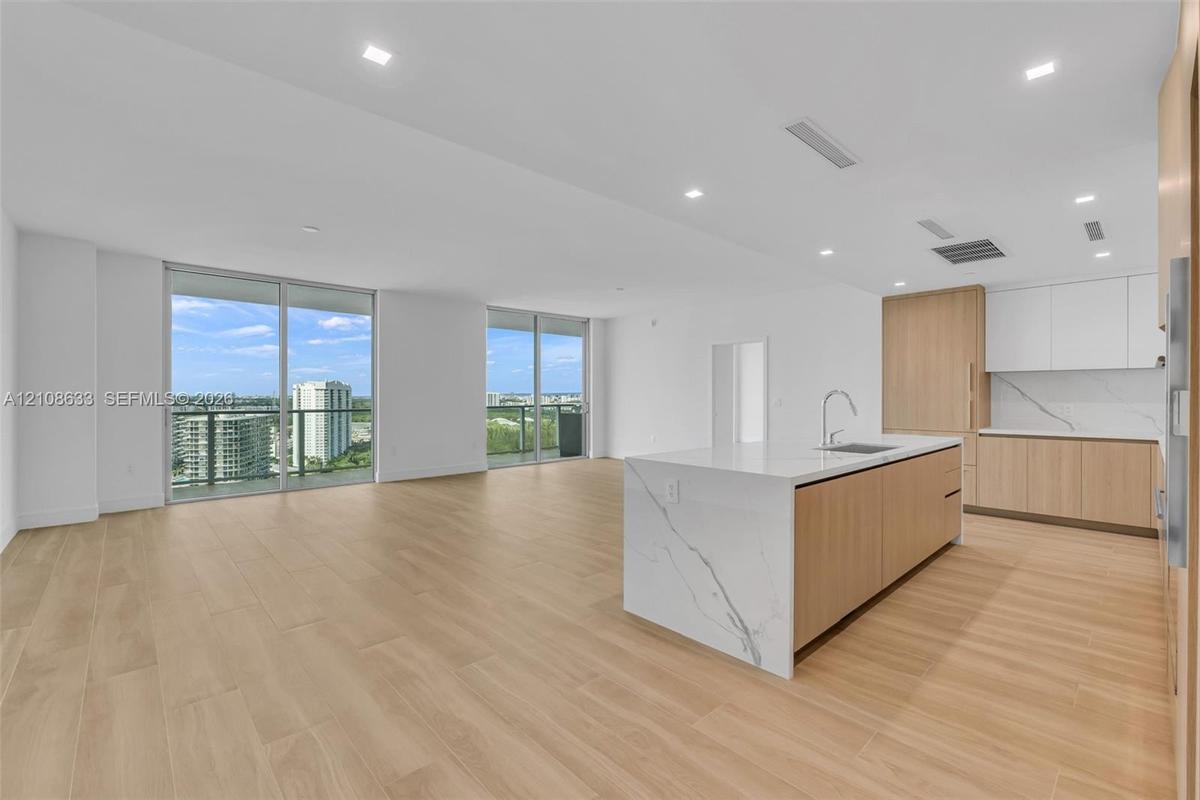 Open-concept interior featuring light wood-finish flooring, a kitchen island with stone-finish waterfall countertop, integrated cabinetry, and floor-t