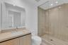 Bathroom featuring a wood-finish vanity with an integrated sink, large frameless wall mirror, walk-in shower with floor-to-ceiling tile, glass enclosu