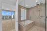 Bathroom featuring floor-to-ceiling large-format tile, glass-enclosed wet room with built-in soaking tub, dual rainfall shower heads, and hand-held sh