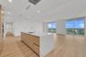 Open-concept kitchen featuring an island with a waterfall-edge countertop, light wood-finish cabinetry, wood-finish flooring, and floor-to-ceiling gla
