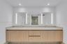 Floating wood-finish vanity with dual integrated sinks, light-toned stone countertop, expansive wall-to-wall mirror with vertical integrated lighting,