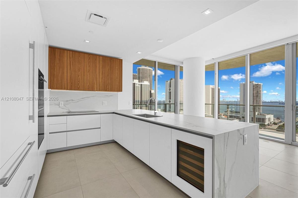 Sleek kitchen featuring white cabinetry, wood-finish upper cabinets, integrated stainless steel appliances, and a central island with a built-in wine 