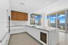 Sleek kitchen featuring white cabinetry, wood-finish upper cabinets, integrated stainless steel appliances, and a central island with a built-in wine 