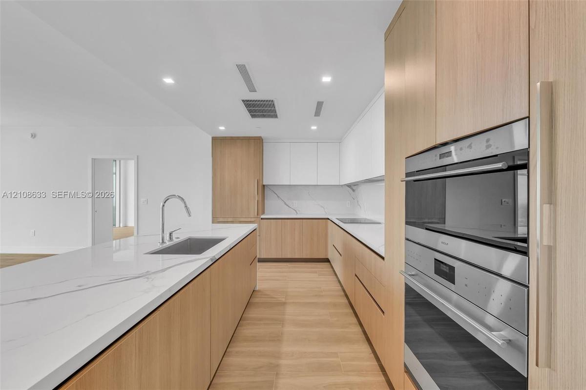 Kitchen featuring wood-finish cabinetry, white stone-look countertops with veining, a stainless steel undermount sink with a gooseneck faucet, and int