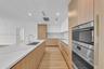 Kitchen featuring wood-finish cabinetry, white stone-look countertops with veining, a stainless steel undermount sink with a gooseneck faucet, and int