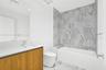Bathroom featuring a floating wood-finish vanity, integrated sink, large format tile flooring, and a tiled shower with an integrated bench