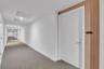 Hallway featuring neutral carpeting, white walls, and a recessed door entry accented with wood-finish paneling and mounted unit signage
