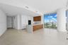 Open concept living area with light-toned tile flooring, floor-to-ceiling windows, and a modern kitchen featuring wood-finish cabinetry, integrated ap