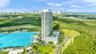High-rise residential tower featuring a multi-level podium, an expansive elevated pool deck, perimeter landscaped grounds, and a coastal lagoon