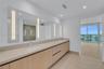 Floating vanity with integrated dual rectangular sinks, light wood-finish cabinetry, full-length illuminated wall mirror, and neutral-tone flooring