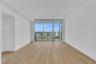 Open-concept interior featuring wood-finish flooring, floor-to-ceiling glass sliding doors, and a private balcony with an urban skyline horizon