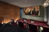 Tiered media room featuring wood-paneled walls, textured accent wall covering, recessed ceiling lighting, and metal handrails