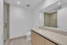 Floating vanity with light wood-finish cabinetry, integrated rectangular sink, large wall-spanning mirror, and glass-enclosed shower with neutral-tone