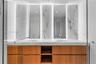 Dual vanity featuring wood-finish cabinetry, integrated sinks, a solid surface countertop, and backlit mirrors with wall-mounted stone-look tiles