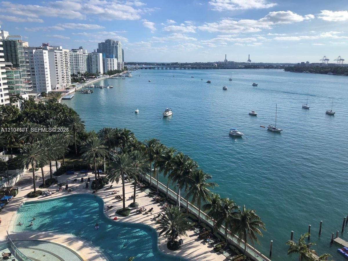 Waterfront grounds featuring a swimming pool, paved sundeck, mature palm trees, and direct access to an open waterway