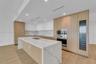 Kitchen featuring wood-finish cabinetry, waterfall-edge island, stone-surfaced countertops and backsplash, integrated oven, and built-in wine refriger