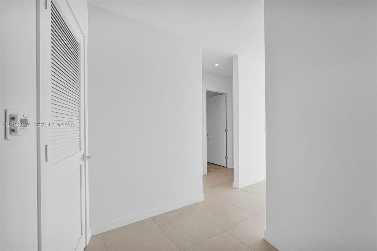 Louvered door, neutral tile flooring, recessed lighting, and crisp white walls