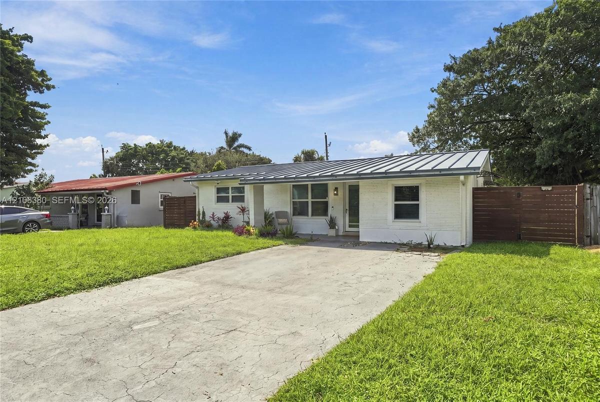 Single-story exterior featuring a painted brick facade, metal roofing, concrete driveway, and wood-slat privacy fencing