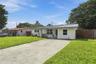 Single-story exterior featuring a painted brick facade, metal roofing, concrete driveway, and wood-slat privacy fencing