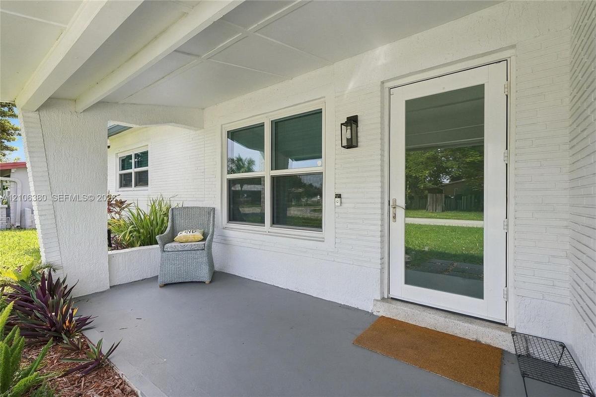 Covered front porch featuring painted brick exterior, concrete flooring, exterior wall-mounted lantern light fixture, and a full-light glass panel ent