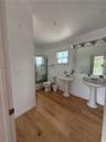 Bathroom featuring wood-finish flooring, dual pedestal sinks, a large wall-mounted mirror with integrated lighting, and a glass-enclosed shower