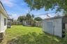 Fenced backyard featuring a grass lawn, detached storage structure, and covered outdoor area