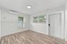 Wood-finish flooring, white walls, dual windows with horizontal blinds, wall-mounted ductless air conditioning unit, and white six-panel exterior door