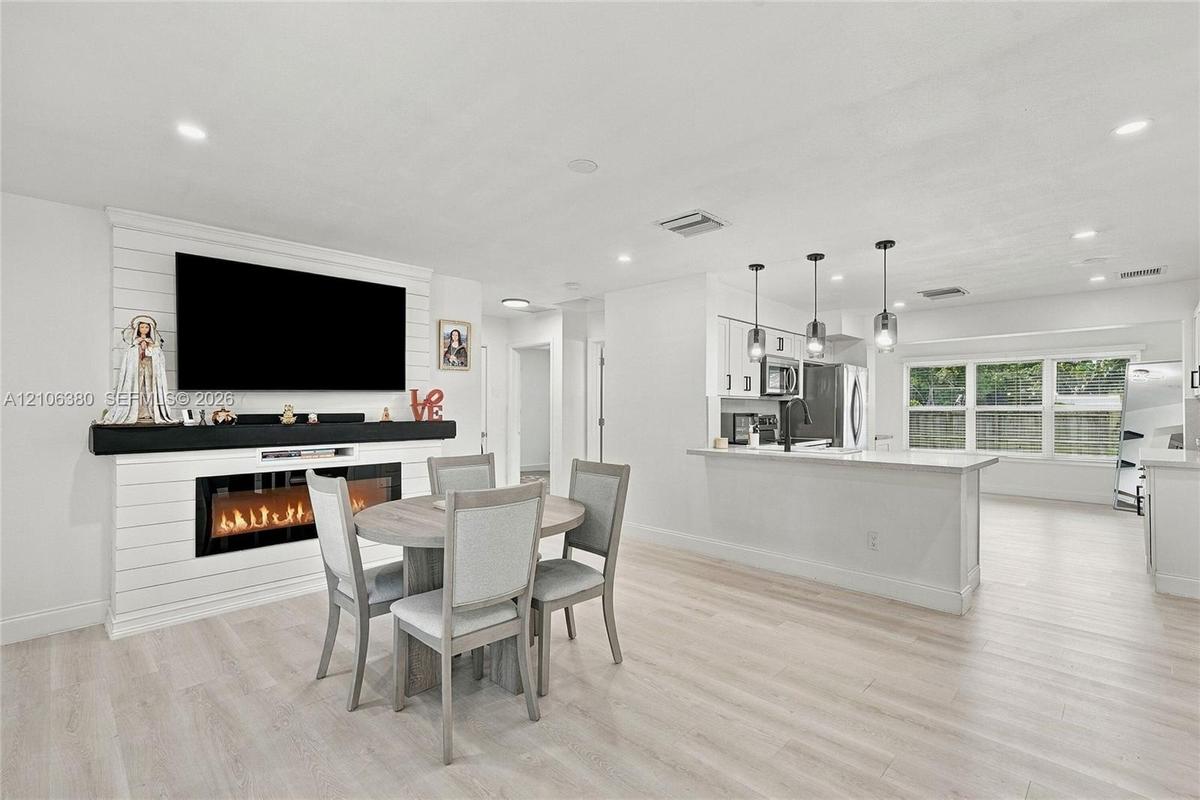 Open-concept interior featuring shiplap fireplace surround, electric fireplace insert, wood-finish flooring, kitchen island with pendant lighting, and