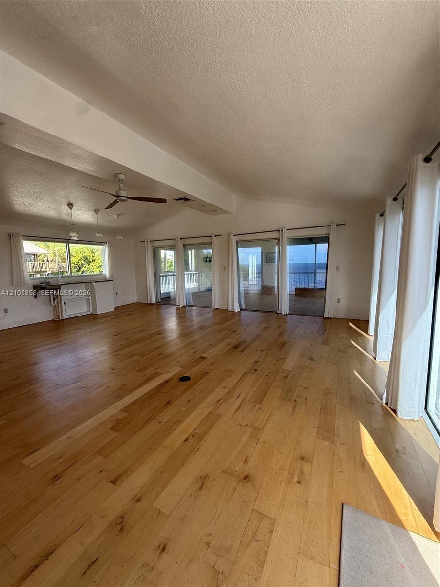 Spacious interior featuring wood-finish flooring, vaulted ceilings, multiple sliding glass doors, a ceiling fan, and built-in cabinetry with a counter