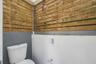 Privacy-fencing enclosure with horizontal wood slats, exposed conduit, and a white porcelain toilet