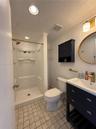 Bathroom featuring a dark-toned vanity with integrated basin, brass-finish fixtures, oval wall mirror, built-in cabinet storage, and a walk-in shower 