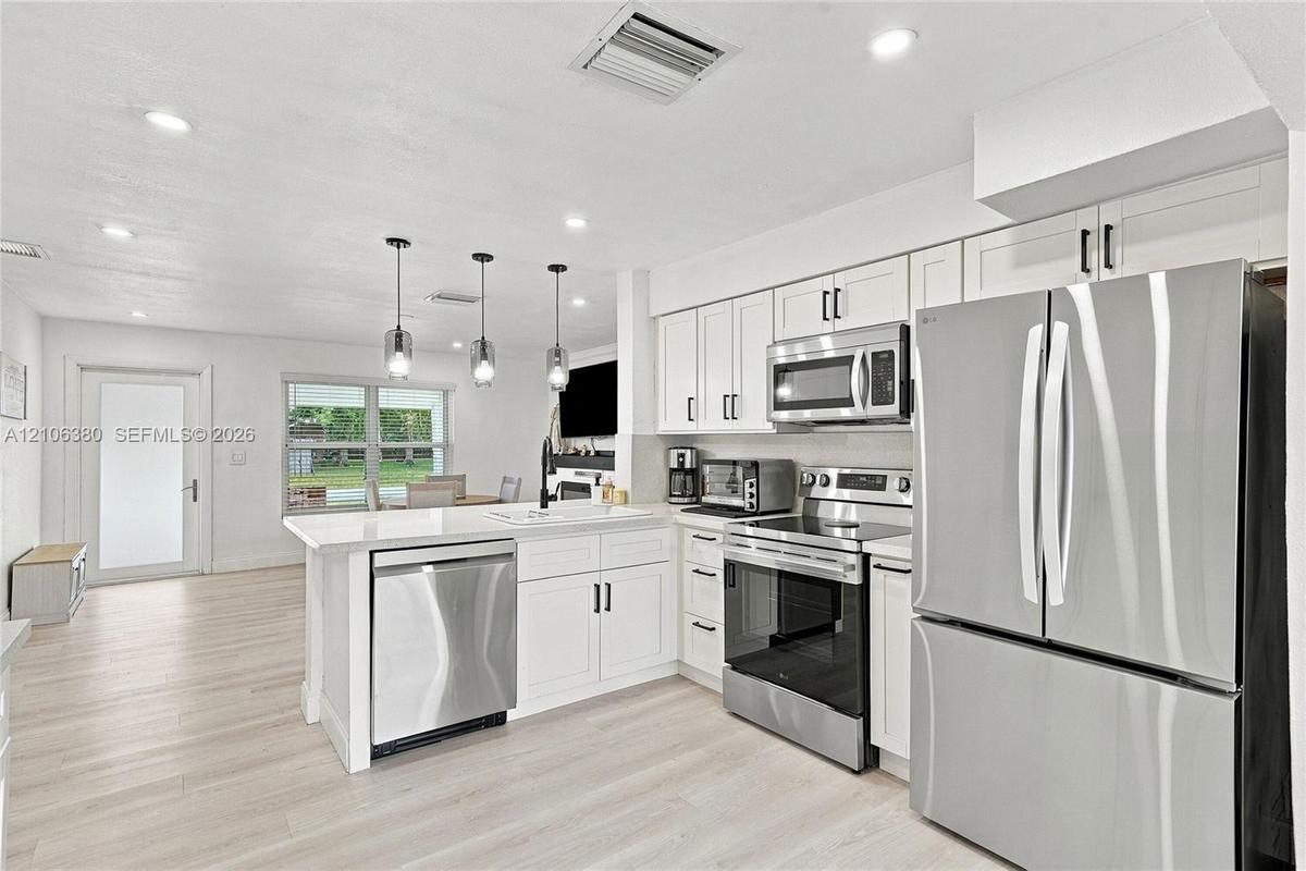 Kitchen featuring white shaker-style cabinetry, stainless steel appliances, quartz countertops, a peninsula with pendant lighting, and light-toned woo