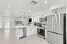 Kitchen featuring white shaker-style cabinetry, stainless steel appliances, quartz countertops, a peninsula with pendant lighting, and light-toned woo