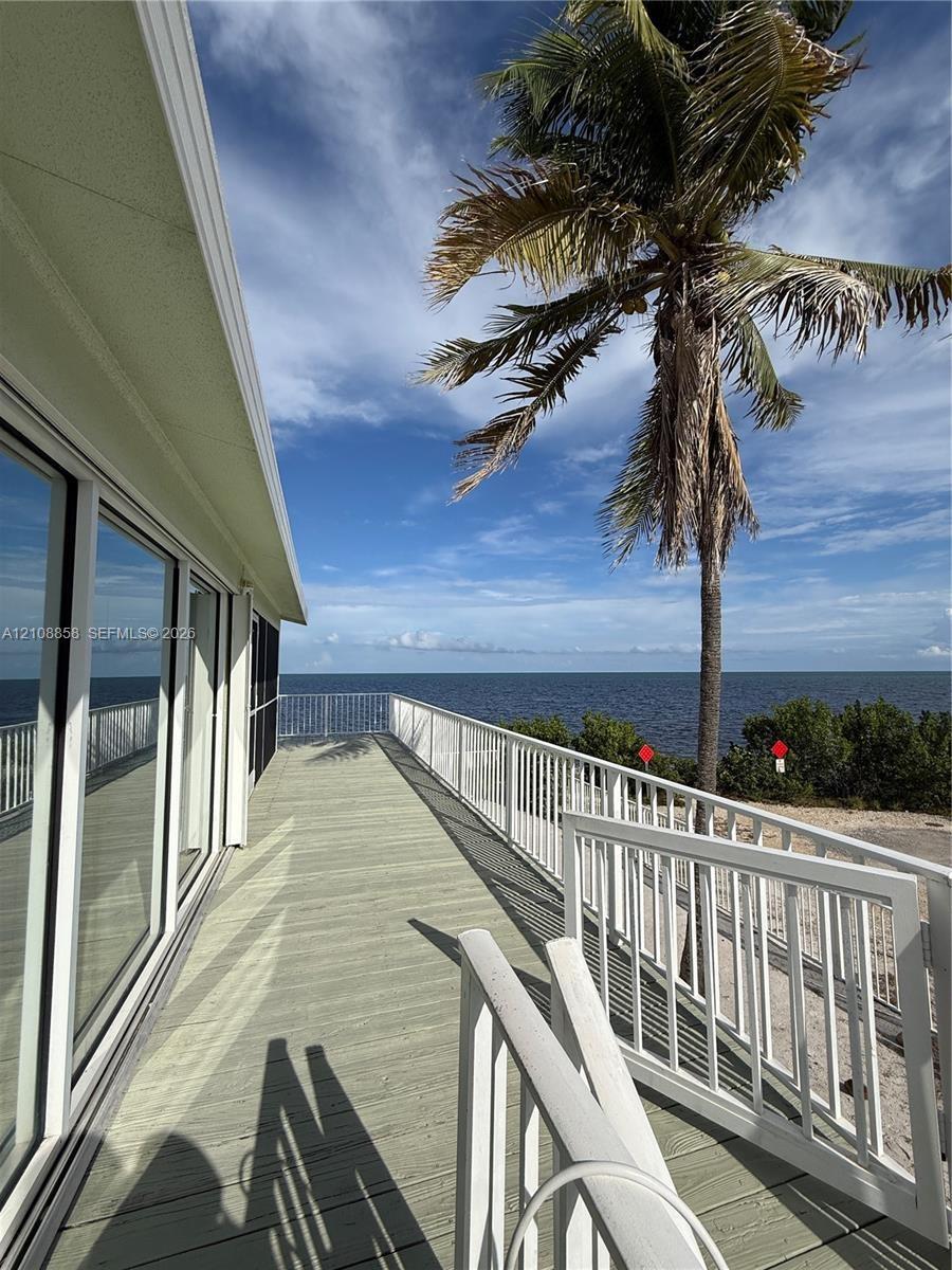 Extended deck featuring composite planking, white metal railings, sliding glass exterior doors, and a waterfront location