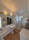 Dual porcelain pedestal sinks, wood-finish flooring, full-width wall mirror, and a tub-shower combination with sliding glass doors