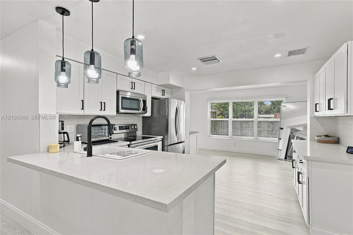 Kitchen featuring white cabinetry, solid-surface countertops, stainless steel appliances, a farmhouse-style sink with a matte black faucet, and glass 