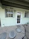 Exterior entry featuring a glass-paneled door, dual grid-style windows, pebble ground cover, and circular concrete pavers