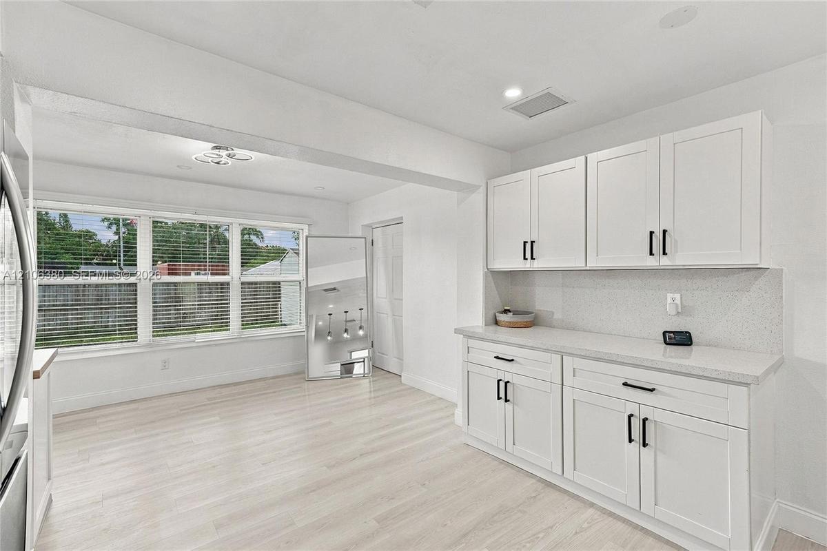 White cabinetry with matte black hardware, stone-finish countertops, light wood-finish flooring, and multi-pane windows