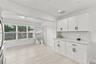 White cabinetry with matte black hardware, stone-finish countertops, light wood-finish flooring, and multi-pane windows