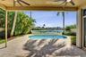 Covered patio featuring paver flooring and ceiling fans, opening to a pool with a metal perimeter fence and mature palm trees