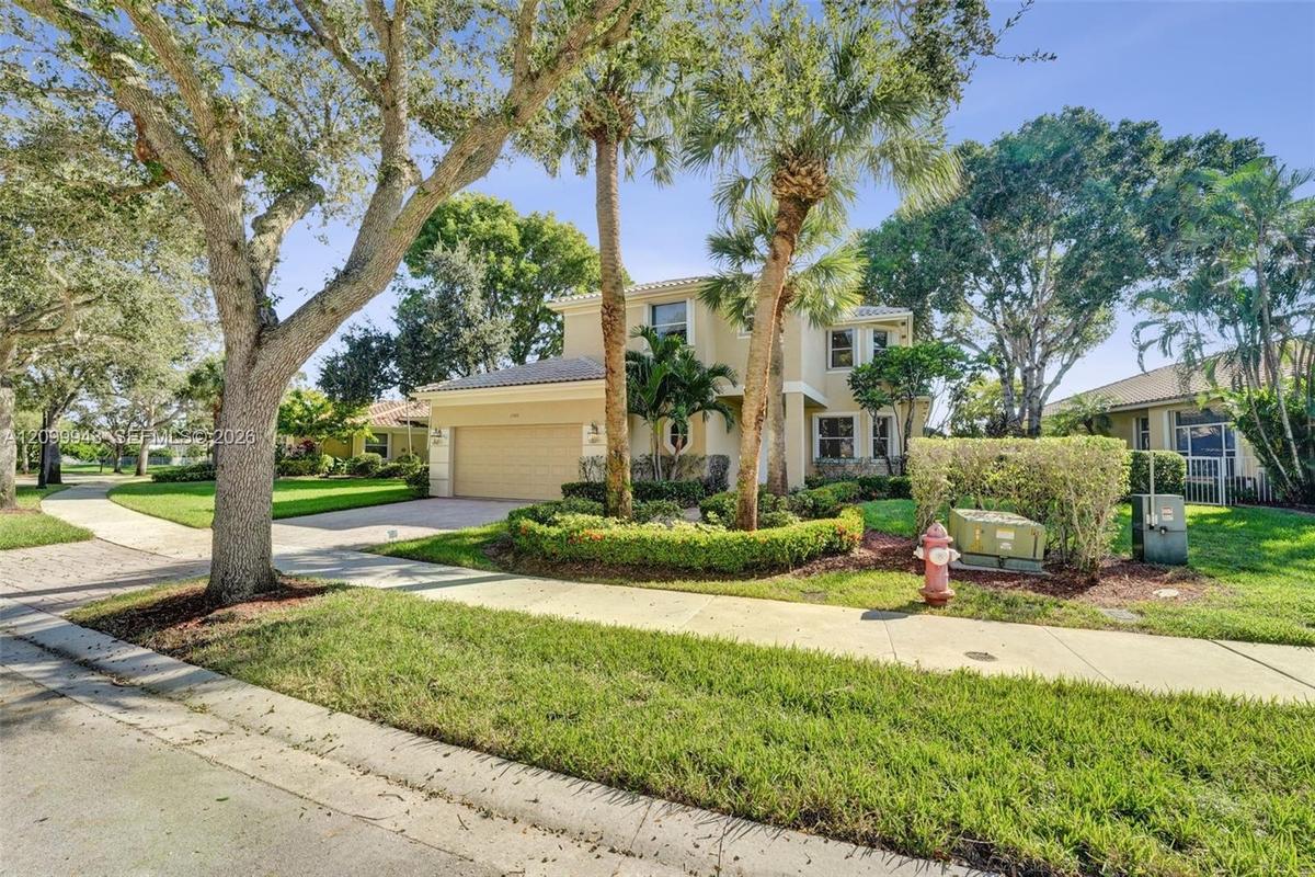 Two-story residence featuring a stucco exterior, integrated two-car garage, manicured landscaping with mature palm trees, and a concrete paver drivewa