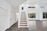 Double-height ceiling, wood-finish flooring, staircase with wood-finish treads, and multiple windows providing natural light