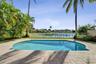 Inground swimming pool with paver decking, enclosed by a perimeter fence, featuring mature palm trees and water frontage