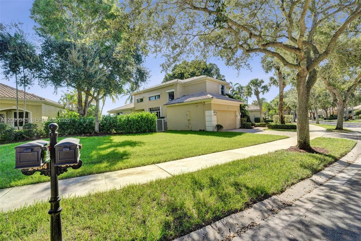 Two-story stucco exterior featuring a tile roof, an attached garage, manicured lawn, and mature canopy trees