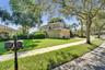 Two-story stucco exterior featuring a tile roof, an attached garage, manicured lawn, and mature canopy trees
