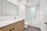 Bathroom featuring a wood-finish vanity, solid surface countertop, rectangular under-mount sink, glass block window, and a shower-tub combination with