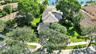 Aerial perspective of a multi-level residence featuring a multi-pitched tile roof, expansive grass lawn, mature shade trees, and waterfront positionin