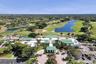 Expansive clubhouse facility featuring a multi-gabled green metal roof, a circular porte-cochère entry, mature palm tree landscaping, and paved parkin