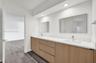 Dual-sink vanity with light-tone wood-finish cabinetry, white countertop, integrated rectangular basins, and wall-mounted mirrors with recessed lighti