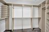 Walk-in closet featuring floor-to-ceiling built-in cabinetry, tiered shelving units, integrated hanging rods, and wood-finish flooring